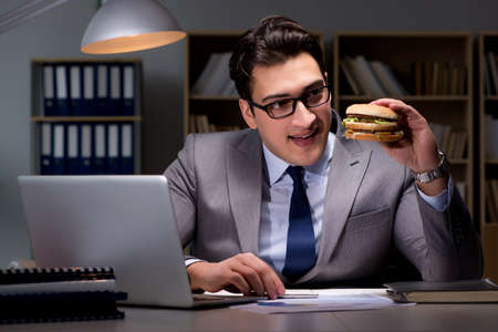 Businessman late at night eating a burgerの写真素材