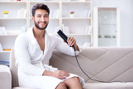 Young man drying hair at home with a hair dryer blowerの写真素材