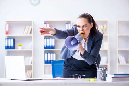 Angry businesswoman yelling with loudspeaker in officeの写真素材