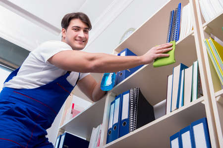 Male office cleaner cleaning shelves in office