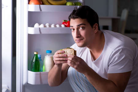 Man at the fridge eating at nightの写真素材