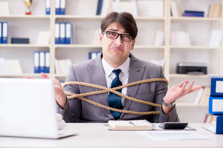 Businessman tied up with rope in officeの写真素材