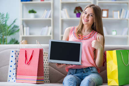 Young woman with shopping bags indoors home on sofaの写真素材