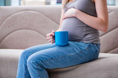 Pregnant woman with a belly tummy sitting on a sofa at homeの写真素材