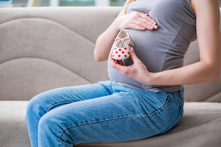 Pregnant woman with a belly tummy sitting on a sofa at home