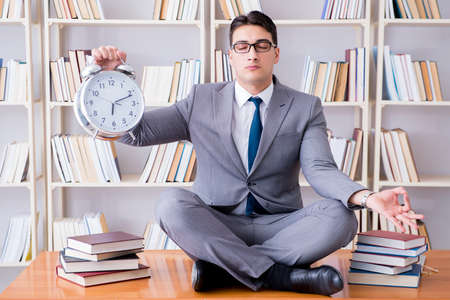 Businessman student in lotus position with an alarm clock in libの写真素材