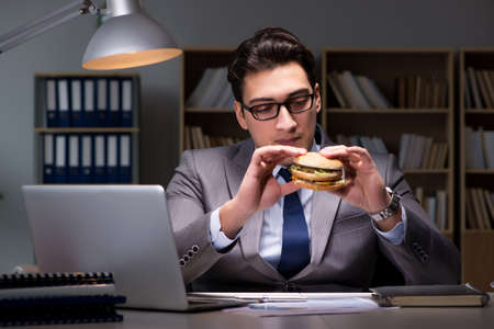 Businessman late at night eating a burgerの写真素材
