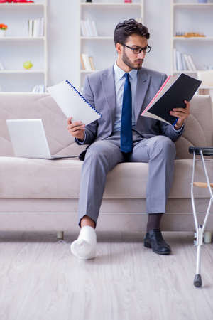 Businessman with crutches and broken leg at home workingの写真素材