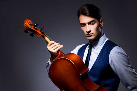 Young man playing cello in dark roomの写真素材