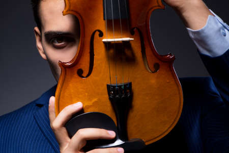 Young man playing violin in dark roomの写真素材
