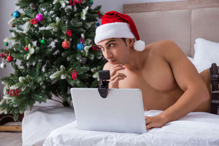 Sexy man in the bed wearing santa hat in christmas conceptの写真素材