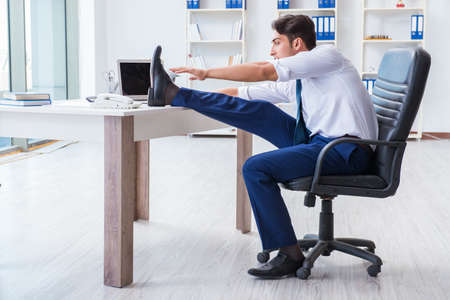 Young businessman doing sports stretching at workplaceの写真素材