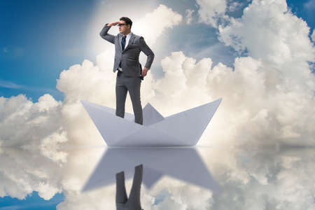 Businessman looking into future with binoculars in paper ship boの写真素材