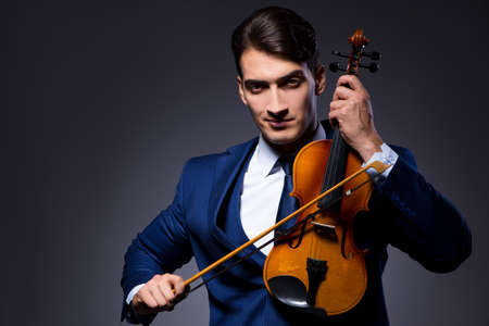 Young man playing violin in dark roomの写真素材