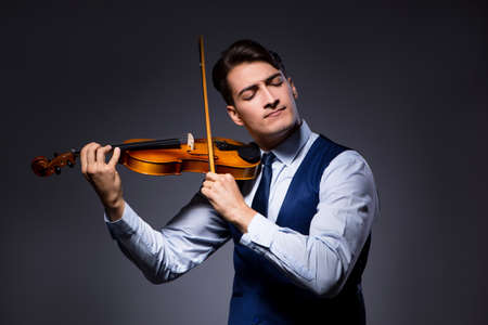 Young man playing violin in dark roomの写真素材