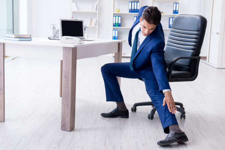 Young businessman doing sports stretching at workplaceの写真素材