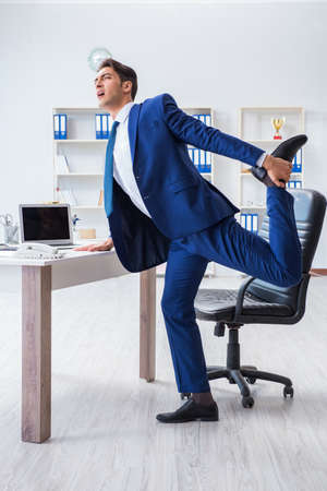 Young businessman doing sports stretching at workplaceの写真素材