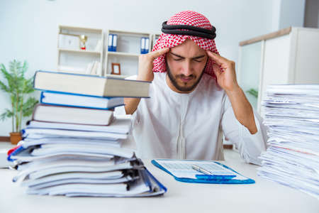 Arab businessman working in the office doing paperwork with a pile of papersの写真素材