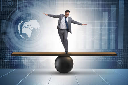 Businessman trying to balance on ball and seesawの写真素材