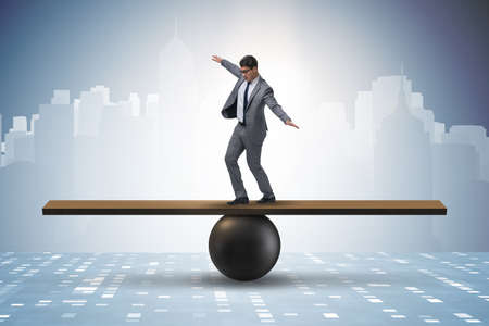 Businessman trying to balance on ball and seesawの写真素材