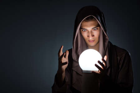 Young wizard with crystal ball in dark roomの写真素材