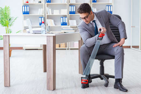 Young businessman exercising with elastic expander in officeの写真素材