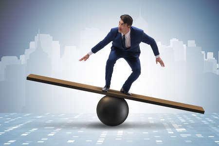 Businessman trying to balance on ball and seesawの写真素材