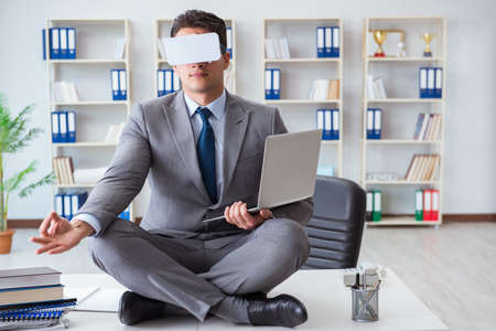 Businessman in virtual reality VR glasses meditating at desk topの写真素材