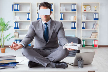 Businessman in virtual reality VR glasses meditating at desk topの写真素材