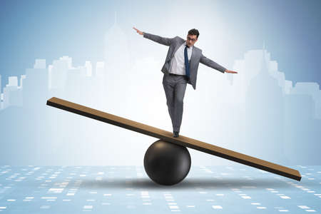 Businessman trying to balance on ball and seesawの写真素材