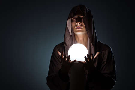 Young wizard with crystal ball in dark room