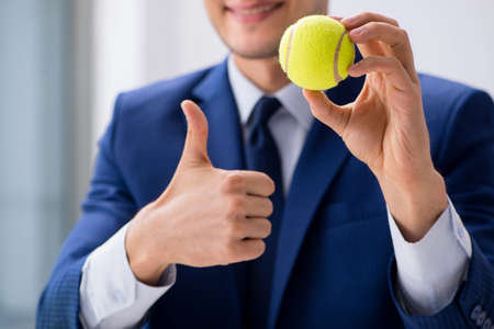 Young businessman with tennis ball working in officeの写真素材