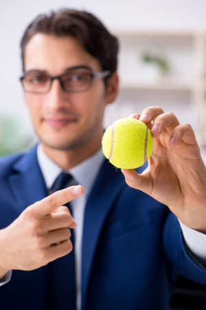 Young businessman with tennis ball working in officeの写真素材