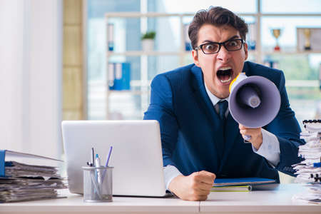 Angry aggressive businessman with bullhorn loudspeaker in officeの写真素材