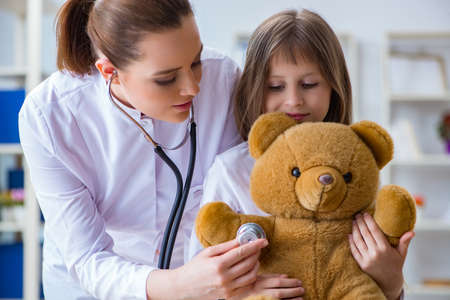 Woman female doctor examining little cute girl with toy bearの写真素材