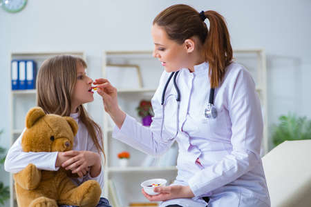 Woman female doctor examining little cute girl with toy bearの写真素材