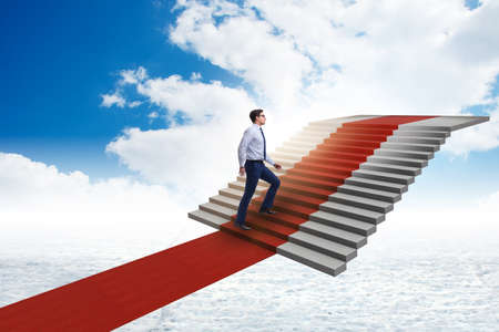Young businessman climbing stairs and red carpet into skyの写真素材