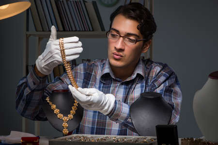 Young male jeweller working at night in his workshopの写真素材