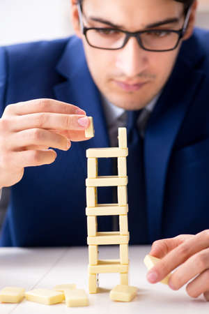 Young businessman building domino tower in officeの写真素材