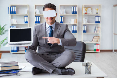 Businessman in virtual reality VR glasses meditating at desk topの写真素材