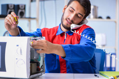 Young repairman fixing and repairing microwave ovenの写真素材
