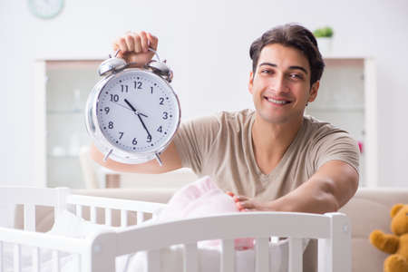 Young dad with clock near newborn baby bed cotの写真素材