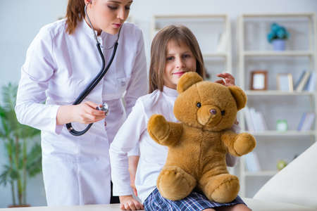 Woman female doctor examining little cute girl with toy bearの写真素材