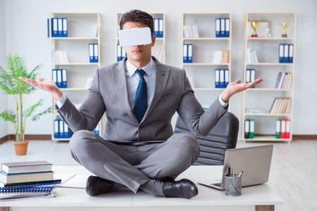 Businessman in virtual reality VR glasses meditating at desk topの写真素材