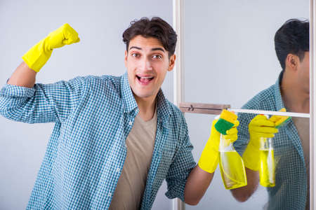 Young man cleaning mirror at home hotelの写真素材