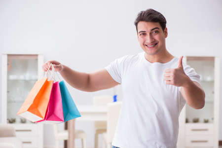 Young man with gift bag at home preparing suprise for wifeの写真素材