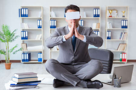 Businessman in virtual reality VR glasses meditating at desk topの写真素材