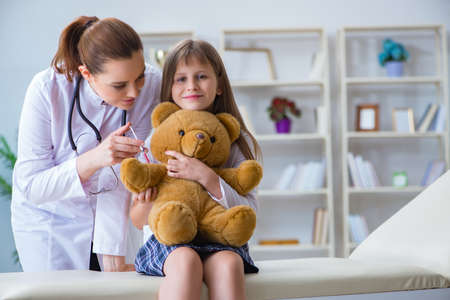 Woman female doctor examining little cute girl with toy bearの写真素材