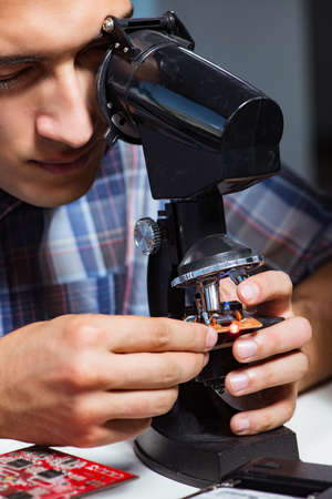 Repairman trying to repair laptop with miscroscope