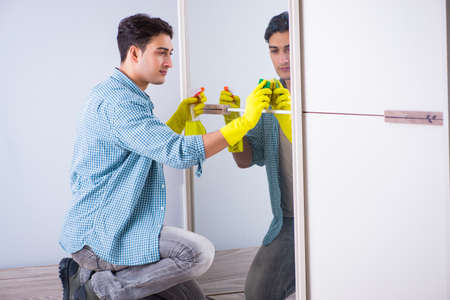 Young man cleaning mirror at hotel roomの写真素材